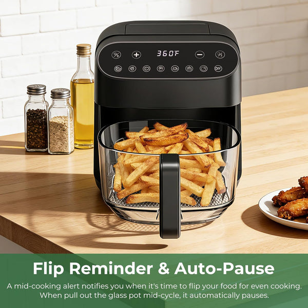 Black air fryer with glass basket containing fries on a wooden countertop.