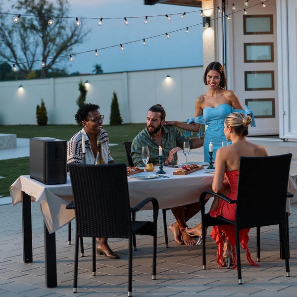 Group of people dining outdoors with string lights and a woman in a blue dress standing behind them.