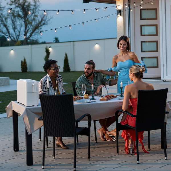 Group of people dining outdoors with string lights and a woman in a blue dress standing behind them.