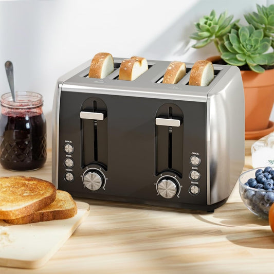 Black toaster with four slices of bread on a wooden table with a plant and jars in the background.